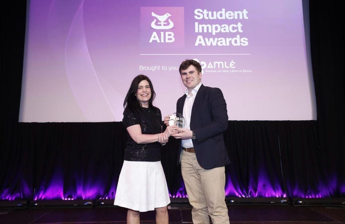 Seán Barrett on stage receiving the award from a presenter, in front of an AIB Student Impact Awards screen.