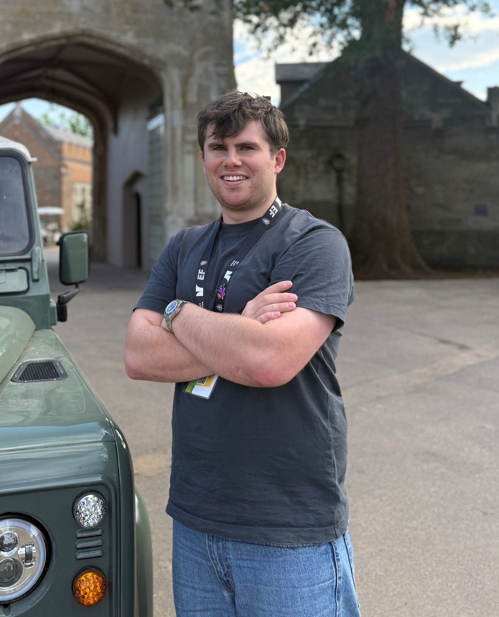 Seán Barrett standing with his arms folded in front of a stone gatehouse, beside a green Land Rover.